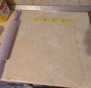 Пласт слоеного теста, нарезанный на 10 полосок. Вдоль одной из них выложены кусочки яблока